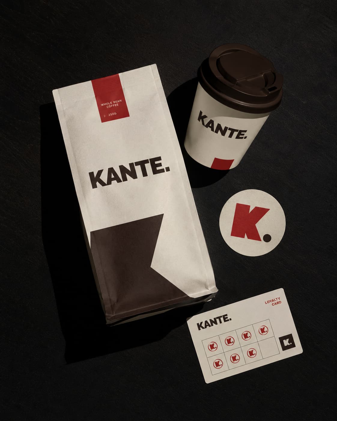 KANTE. Packaging-System: Coffee Bag, Cup, Sticker und Loyalty Card gemeinsam arrangiert, hartes Top-Light auf Warmschwarz.